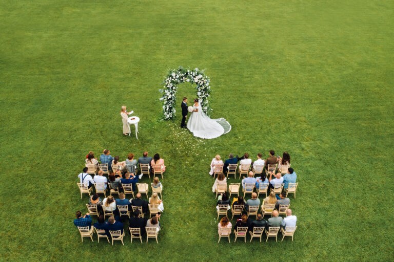 Top view of the Wedding ceremony in a green field with guests sitting on chairs. Wedding venue on the green lawn